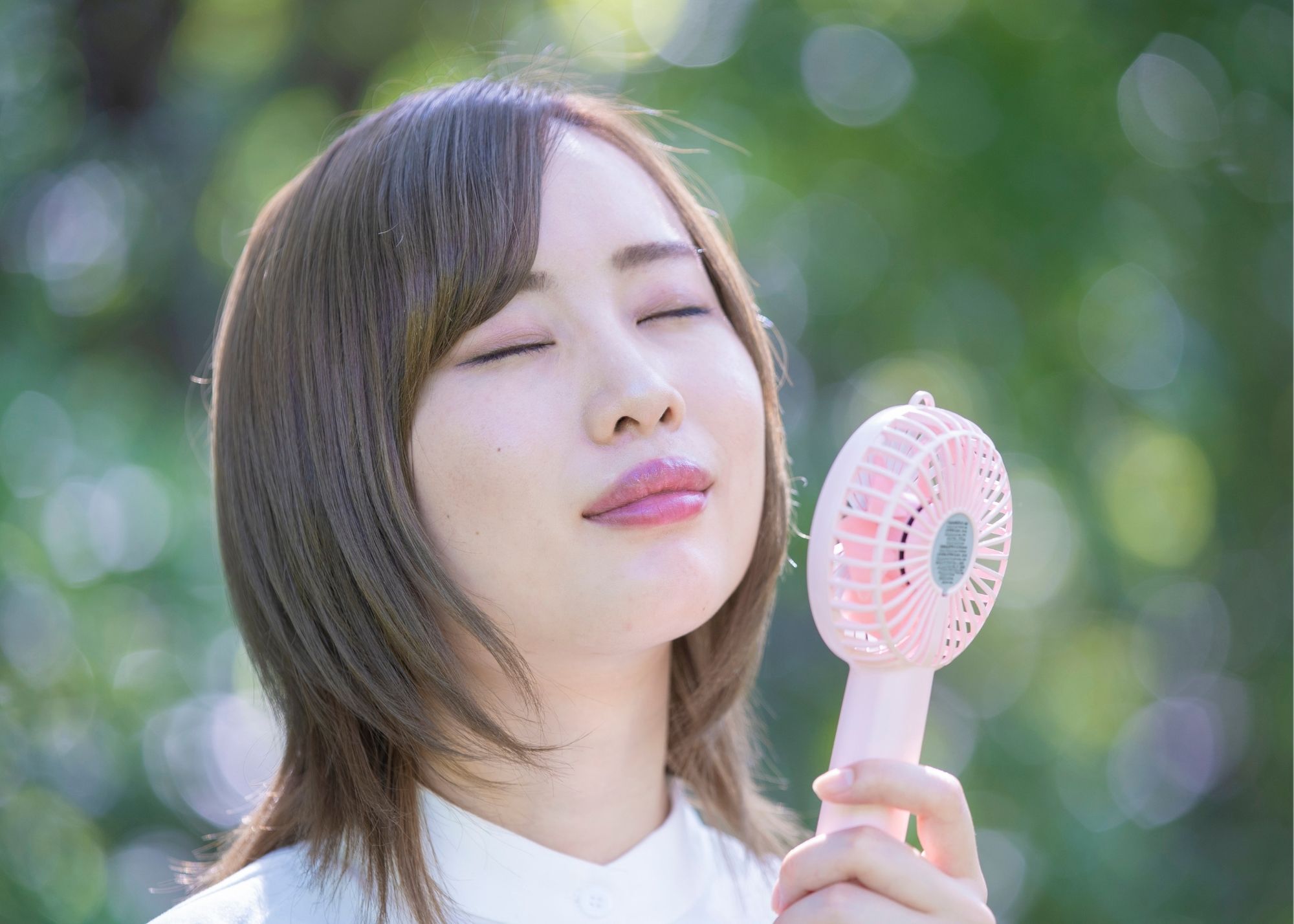 brunette holding a pink travel fan up to her face to cool down, travel fan