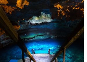 Devil's Den Florida, pov of photo is walking down stairs into the spring that's dark and lit up at the center from the sky above coming through the hole in the top of the spring